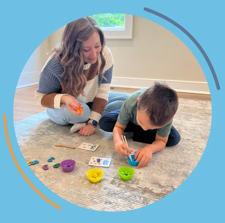 A smiling therapist helping a young boy paint during an ABA therapy activity.